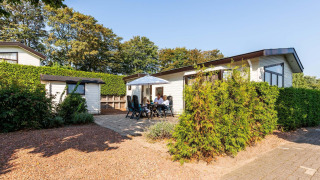 Feriehytte ved EuroParcs Noordwijkse Duinen i Holland med mennesker der nyder terrassen i solskin.