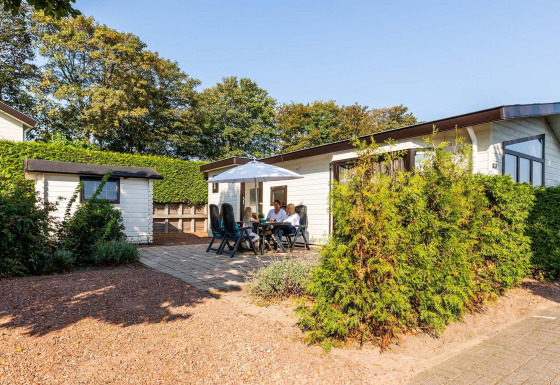 Feriehytte ved EuroParcs Noordwijkse Duinen i Holland med mennesker der nyder terrassen i solskin.