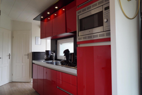 Moderne Küche mit roten Schränken, Einbaugeräten und Fenster in einer Ferienwohnung bei EuroParcs Noordwijkse Duinen.