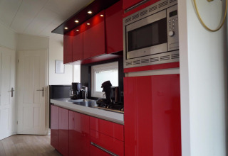 Cocina moderna con armarios rojos, electrodomésticos integrados y ventana en una casa de vacaciones en EuroParcs Noordwijkse Duinen.