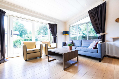 Helles, modernes Wohnzimmer im Ferienhaus bei EuroParcs Noordwijkse Duinen mit großer Fensterfront und stilvollen Möbeln.