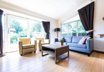 Helles, modernes Wohnzimmer im Ferienhaus bei EuroParcs Noordwijkse Duinen mit großer Fensterfront und stilvollen Möbeln.