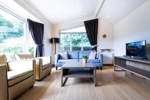 Helles Wohnzimmer einer Hütte im EuroParcs Noordwijkse Duinen mit Sofa, Sessel und großem Fenster.
