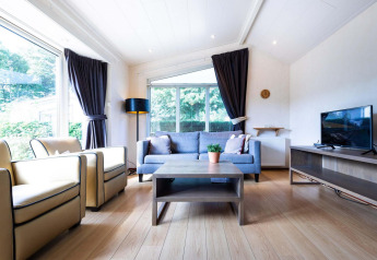 Lyst opholdsområde i træhytte på EuroParcs Noordwijkse Duinen med store vinduer, sofa og tv.