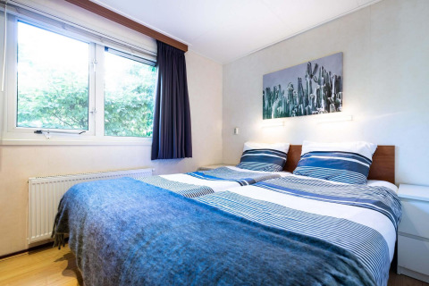 Dormitorio luminoso en casa de vacaciones en EuroParcs Noordwijkse Duinen, con dos camas y una gran ventana.