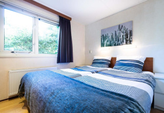 Chambre lumineuse dans une maison de vacances à EuroParcs Noordwijkse Duinen, avec deux lits simples et une grande fenêtre.