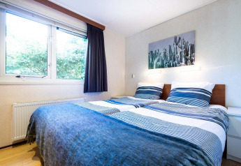 Dormitorio luminoso en casa de vacaciones en EuroParcs Noordwijkse Duinen, con dos camas y una gran ventana.