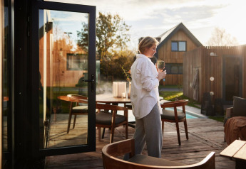 Donna che si gode una bevanda sulla terrazza in legno alla Unbrick One Lodge con sauna e piscina a De Weelderik, Paesi Bassi.