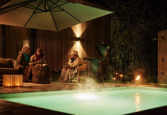 Tre persone rilassate sedute vicino alla piscina riscaldata di Unbrick One Lodge durante una serata fresca.