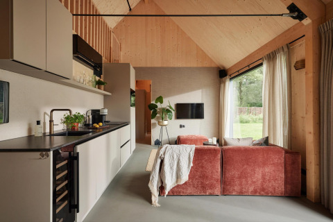 Modern lodge interior featuring a compact kitchen, red sofa, large windows, and wooden vaulted ceiling.
