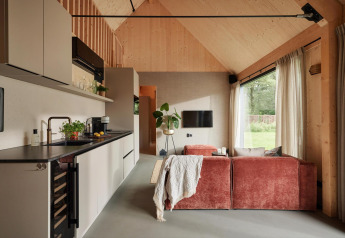 Intérieur moderne d’un lodge avec cuisine compacte, canapé rouge, grandes fenêtres et plafond en bois.