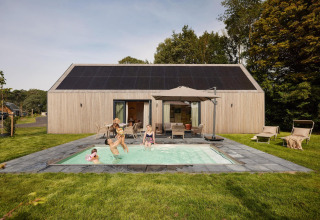 Une famille profite d'une piscine extérieure devant un lodge moderne avec des panneaux solaires sur le toit.