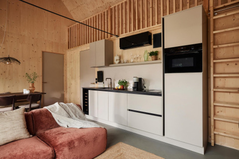 Cocina moderna en una cabaña con paneles de madera, electrodomésticos y una zona de estar acogedora.