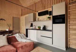 Cocina moderna en una cabaña con paneles de madera, electrodomésticos y una zona de estar acogedora.