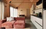 Refugio moderno con cocina abierta, paredes de madera, sofá rosa y comedor junto a ventanales amplios.