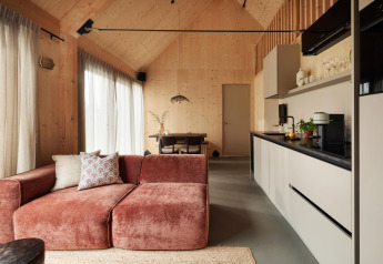 Lodge moderna con cucina aperta, pareti in legno, divano rosa, grandi finestre e zona pranzo.