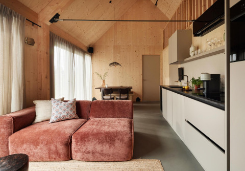 Moderne lodge met open keuken, houten wanden, roze bank, grote ramen met gordijnen en eethoek.