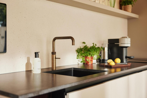 Cocina moderna de lodge con grifo dorado, cafetera, hierbas en maceta y limones sobre la encimera.
