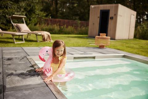 Niña con bañador amarillo y flotador de flamenco rosa jugando en la piscina de Unbrick One, De Weelderik, Países Bajos.