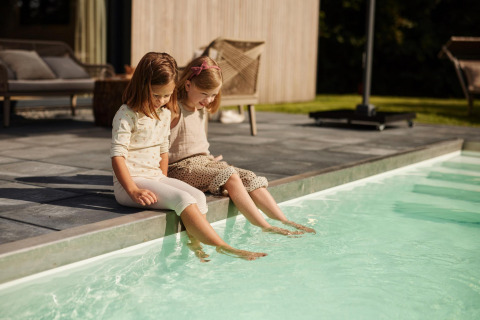 Dos niñas se sientan al borde de una piscina en un lodge y meten los pies en el agua en un día soleado.