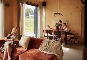 Een gezin beleeft een gezellige tijd in een moderne lodge met houten muren; een vrouw zit ontspannen op de bank.