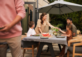 Familia disfruta de una comida al aire libre bajo una sombrilla en un lodge, sonrientes y tranquilos.