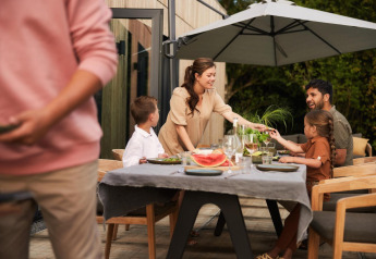 Famille prenant un repas en plein air sous un parasol dans un lodge, souriante et détendue.