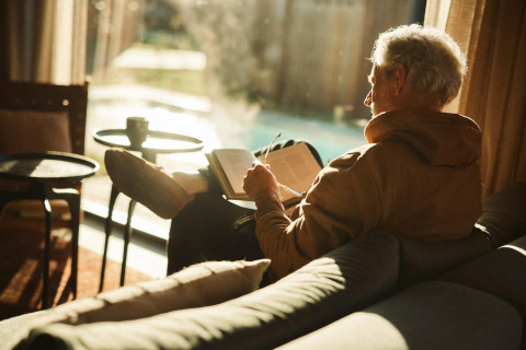Older man reading a book and relaxing in sunlight at Unbrick One | Sauna and Pool lodge in the Netherlands.