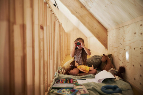 Niña jugando con juguetes y mirando por binoculares en una acogedora cabaña de madera.