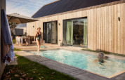 Udendørs scene ved Unbrick One lodge med personer ved pool og solterrasse, træfacade og moderne design.
