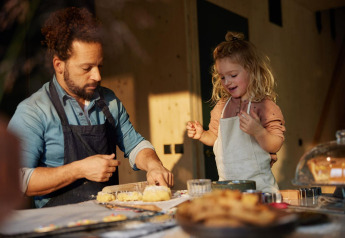 Father and daughter bake together in a cozy lodge kitchen, both wearing aprons and enjoying the moment.
