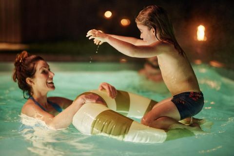 En mor og datter leger sammen i en oplyst pool om aftenen ved Unbrick One Family | Sauna and Pool i De Weelderik, Holland.