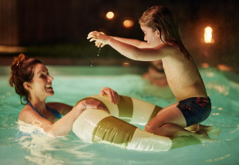 A mother and daughter are playing joyfully in the illuminated pool at Unbrick One Family | Sauna and Pool in De Weelderik, Netherlands.