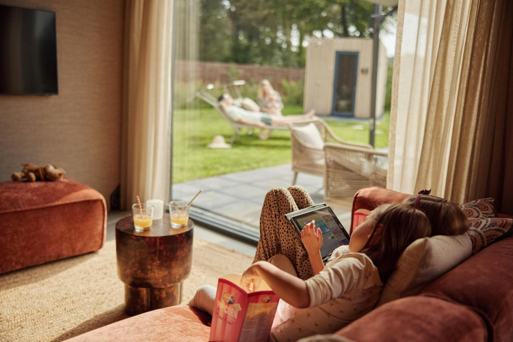 Ein Kind entspannt sich mit einem Tablet auf dem Sofa, während Erwachsene draußen bei Unbrick One Family entspannen.