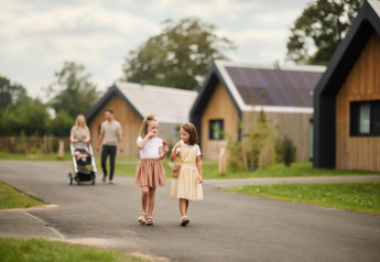 Dos niños comen helado fuera del Unbrick One Family Lodge en De Weelderik, Países Bajos, con padres detrás.