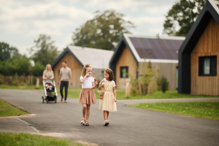 Zwei Kinder essen Eis vor Unbrick One Family Lodge im De Weelderik, Niederlande, während Eltern folgen.