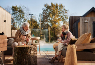Pareja mayor disfruta vino en Unbrick One | Sauna y Pool en De Weelderik, Países Bajos, terraza exterior.