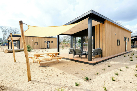 Sand Lodge Sauna, tiny house op Holiday Park De IJsvogel in Nederland, met terras, zand en zonnedoek.