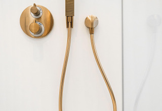 Modern brass shower fixture on a white wall at Unbrick One | Sauna and Pool at De Weelderik in the Netherlands.