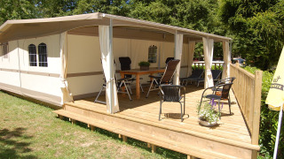 Tenda safari glamping Cahors a La Draille in Francia, con ampia veranda in legno e sedie da giardino.