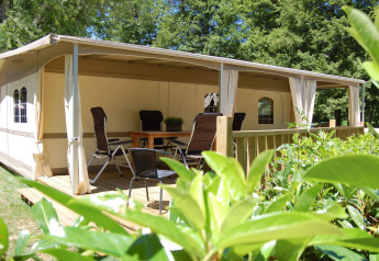 Udendørs terrasse med borde og stole foran en safari-glampingtelt på La Draille i Cahors, Frankrig.