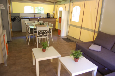 Interior de una tienda safari glamping en La Draille, Francia, con cocina, comedor, sofá y mesas auxiliares.