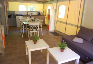Interior de una tienda safari glamping en La Draille, Francia, con cocina, comedor, sofá y mesas auxiliares.