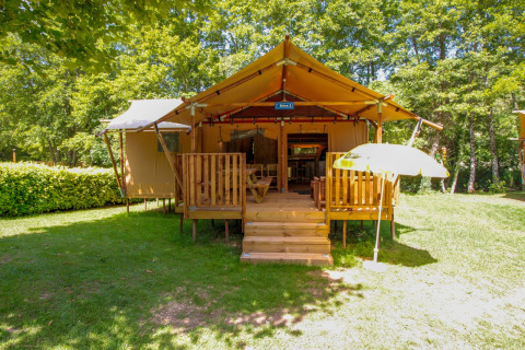 Tienda safari Lodgetent Brive en La Draille, Francia, con terraza de madera y sombrilla rodeada de bosque.