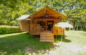 Tienda safari Lodgetent Brive en La Draille, Francia, con terraza de madera y sombrilla rodeada de bosque.