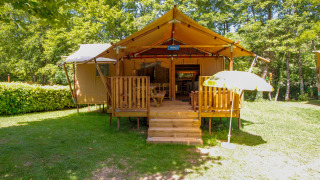 Tienda safari Lodgetent Brive en La Draille, Francia, con terraza de madera y sombrilla rodeada de bosque.