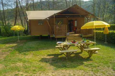 Safari tent Lodgetent Brive at La Draille in France, with a picnic table and yellow umbrellas outside.