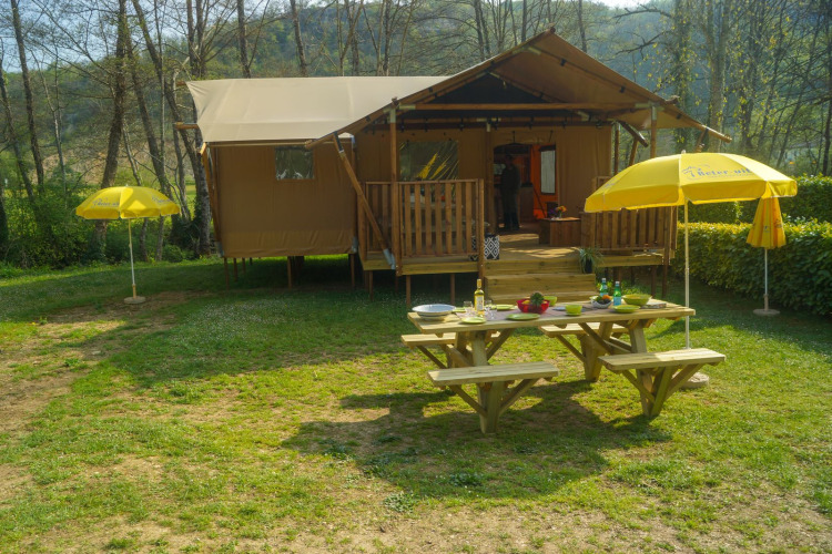 Tienda safari Lodgetent Brive en La Draille, Francia, con mesa de picnic y sombrillas amarillas fuera.