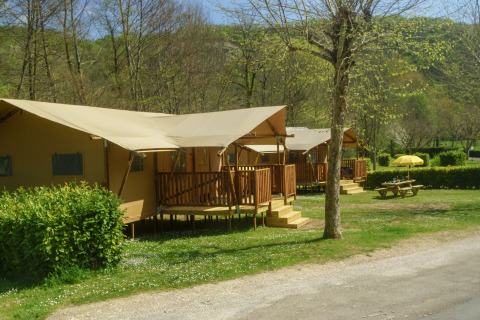 Safari tent Lodgetent Brive at La Draille in France, featuring a wooden deck and picnic table on grassy site.