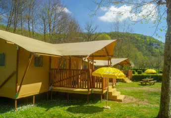 Safari tent Lodgetent Brive at La Draille, France, with porch, yellow umbrellas, and scenic green landscape.